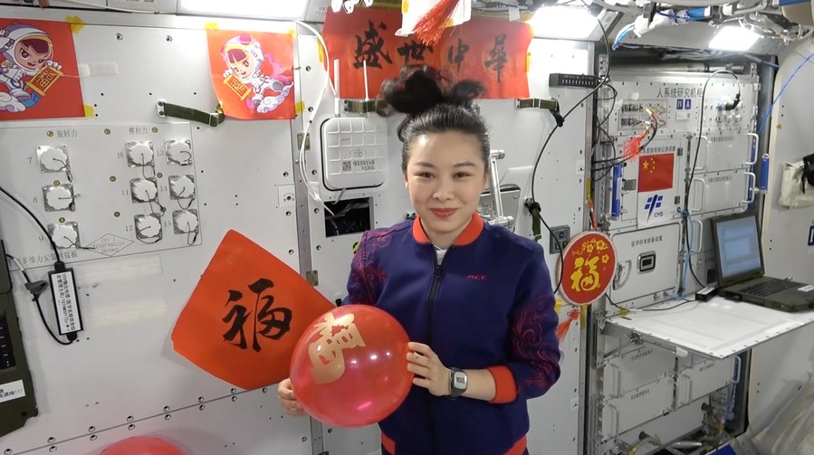 La taikonauta Wang Yaping, vestita a festa, augura ai bambini di tutta la Cina "una crescita vigorosa e sana" mentre tiene in mano un palloncino rosso. (Xinhua)