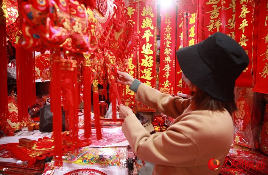 Una cliente seleziona nodi cinesi in un negozio all'interno del tempio del dio della città di Xi'an, nel quale sono in vendita una varietà di decorazioni di Capodanno come carta intagliata per le finestre per l'anno del coniglio. (10 gennaio 2023 - Quotidiano del Popolo Online/Jia Kailu)