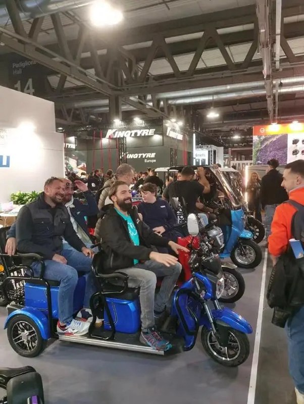 Visitatori all'EICMA provano i tricicli elettrici cinesi.