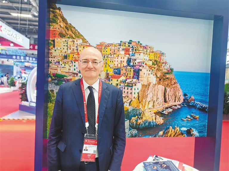 Massimiliano Cozzani posa per una foto davanti a un'immagine della sua città natale presso il padiglione della Regione Liguria alla CISCE. (Hainan Daily/Chen Mingyan)