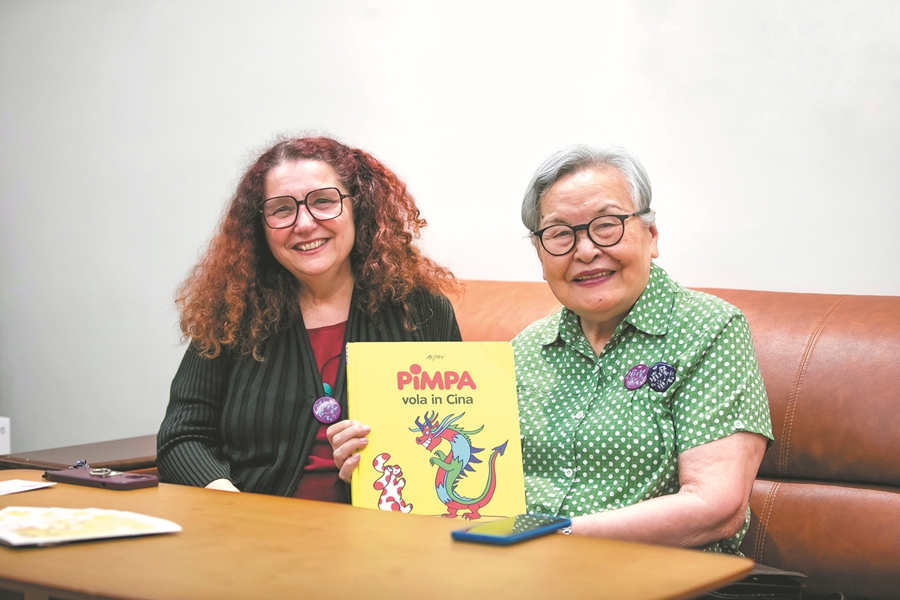 La sinologa italiana Sabrina Ardizzoni (a sinistra) e la direttrice d'orchestra cinese Zheng Xiaoying posano con il libro per bambini Pimpa vola in Cina. (Foto fornita a China Daily)