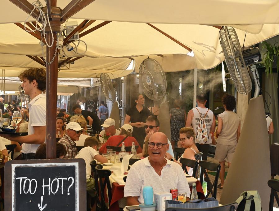 Dei turisti pranzano davanti a un ventilatore per rinfrescarsi a Verona. (2 agosto 2026 - Alberto Lingria/Xinhua)